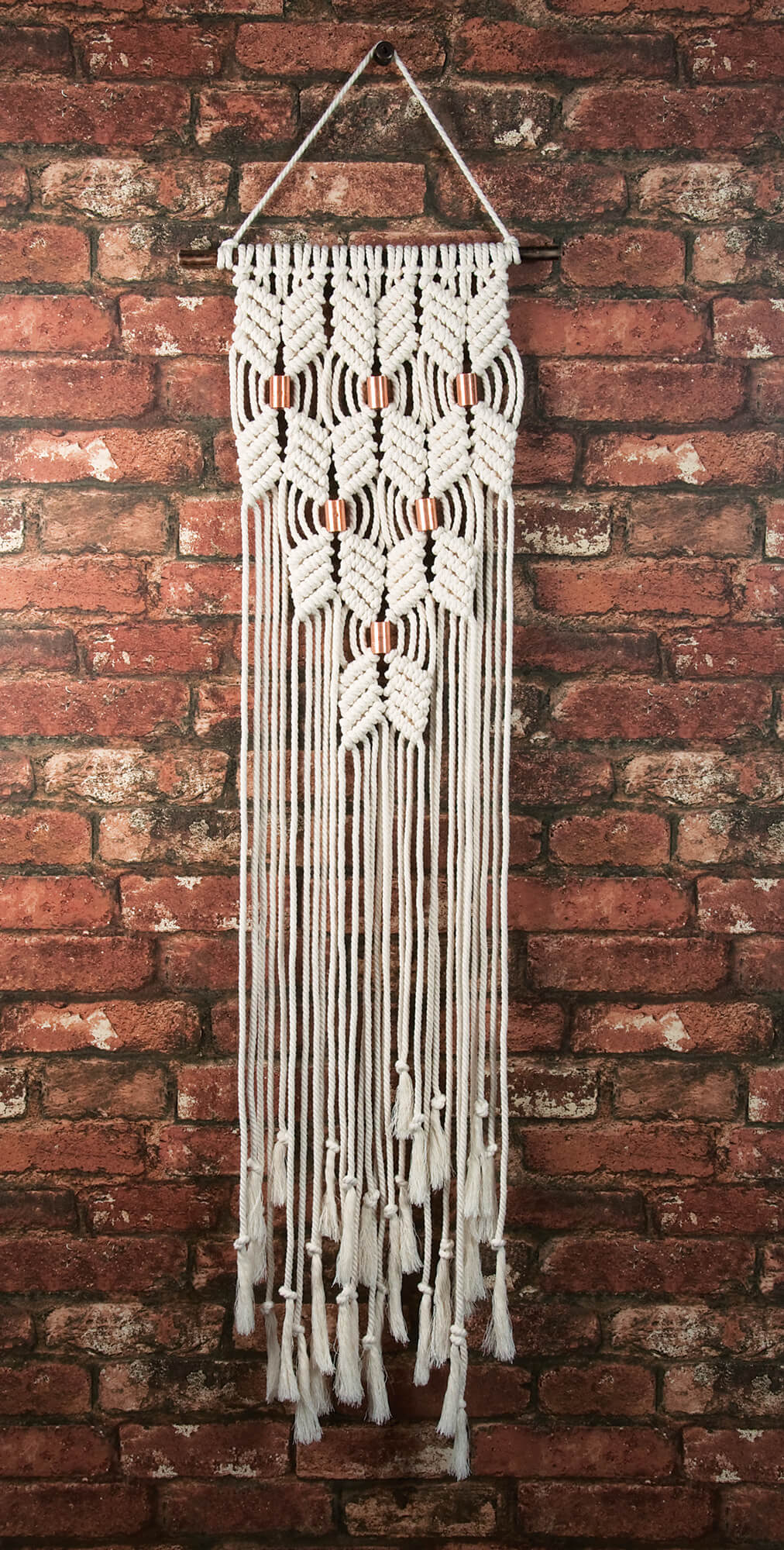 DIY macrame wall hanging kit made up - Chevrons design with coppery finish metal tube accents. shown on brick wall